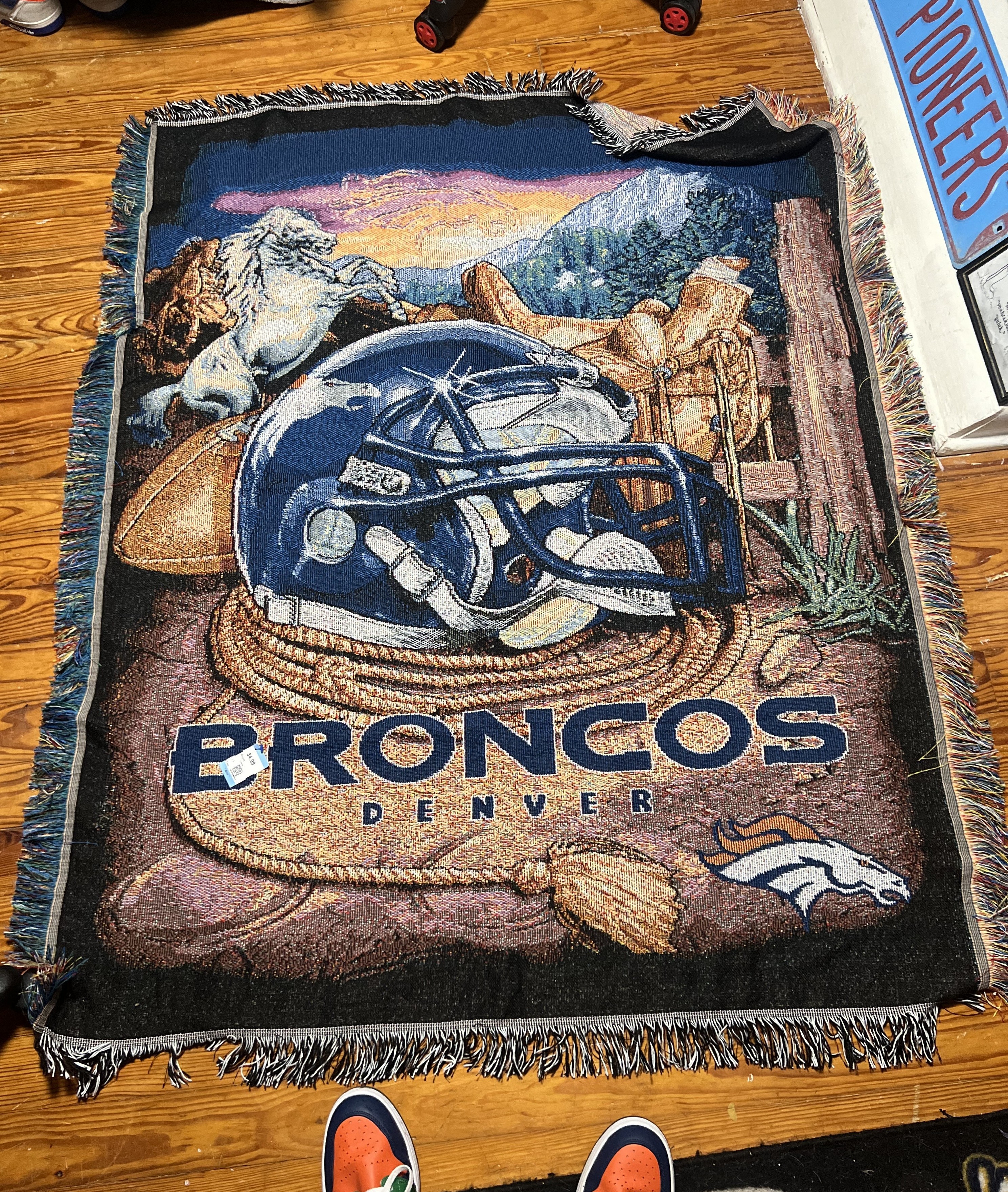 A photo of a vintage knitted Denver Broncos blanket, with older logos and designs. 